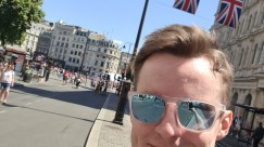Selfie with the medal after running the London 10K - A picture of myself (Luc Shelton) posing with my medal after running the ASICS London 10K. Behind me is a string of Union Jack flags hanging across the street next to Trafalgar Square.